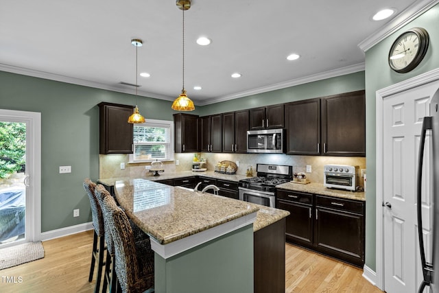 kitchen with appliances with stainless steel finishes, hanging light fixtures, a center island, light stone countertops, and a kitchen bar