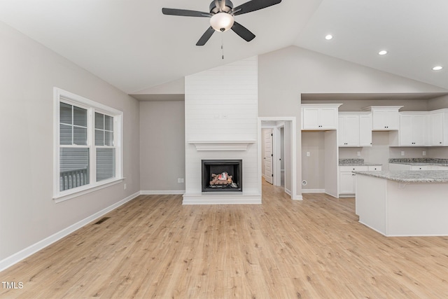 unfurnished living room with vaulted ceiling, ceiling fan, a fireplace, and light wood-type flooring