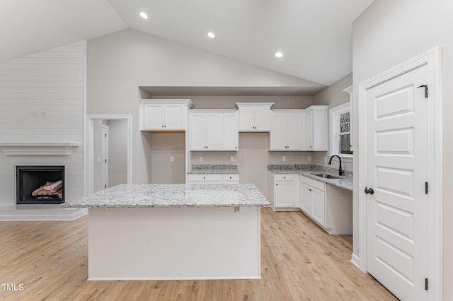 kitchen featuring white cabinetry, a center island, sink, and light stone countertops