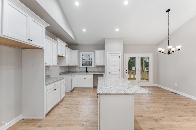 kitchen with sink, light stone countertops, a center island, and white cabinets