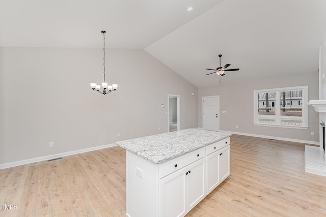 kitchen with a center island, pendant lighting, light stone countertops, ceiling fan with notable chandelier, and white cabinets