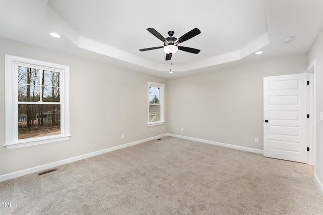 unfurnished room featuring light carpet, a tray ceiling, and ceiling fan