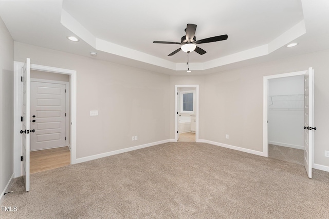 unfurnished bedroom featuring ensuite bathroom, a walk in closet, a raised ceiling, a closet, and light colored carpet