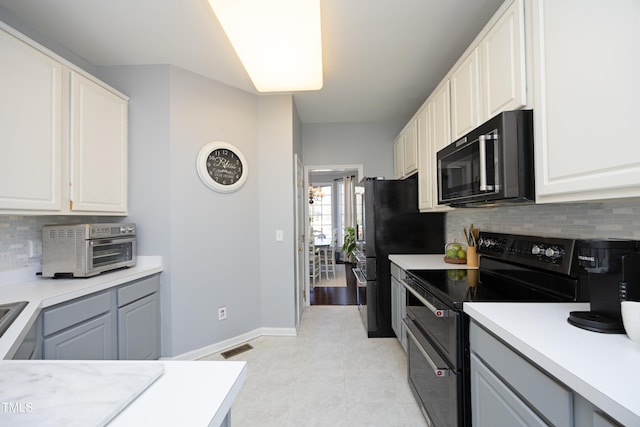 kitchen featuring light tile patterned floors, gray cabinetry, black appliances, white cabinets, and decorative backsplash