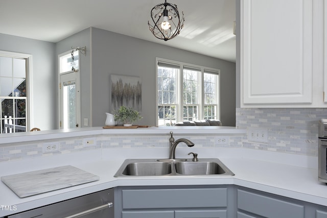 kitchen featuring decorative light fixtures, dishwasher, sink, white cabinets, and backsplash