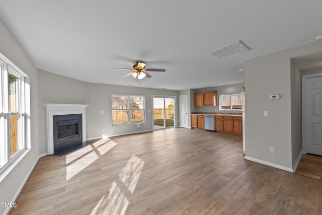 unfurnished living room with a fireplace, light wood finished floors, visible vents, a sink, and baseboards