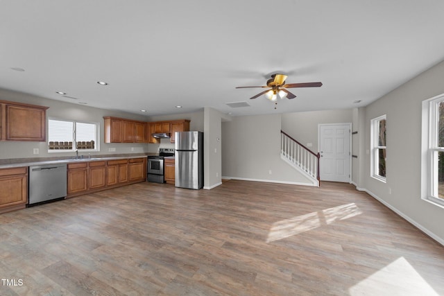 kitchen with baseboards, light wood-style floors, appliances with stainless steel finishes, brown cabinets, and under cabinet range hood