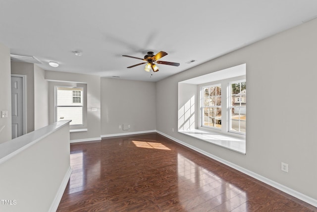 empty room with ceiling fan, visible vents, baseboards, and dark wood-style flooring