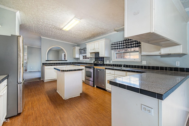 kitchen featuring a textured ceiling, white cabinets, a kitchen island, stainless steel appliances, and ornamental molding