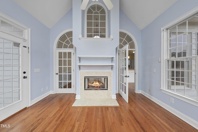 unfurnished living room with hardwood / wood-style flooring, vaulted ceiling, a high end fireplace, and french doors