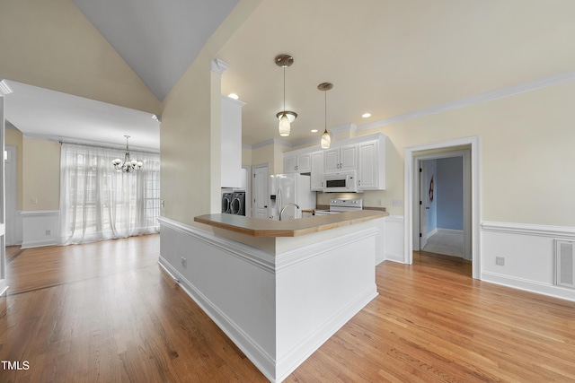 kitchen featuring white appliances, white cabinetry, hanging light fixtures, a notable chandelier, and kitchen peninsula