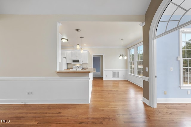 unfurnished living room with ornamental molding, sink, a chandelier, and light hardwood / wood-style floors