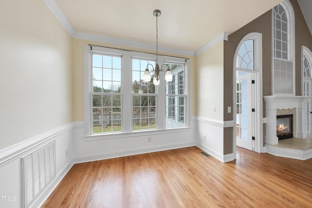 unfurnished dining area with an inviting chandelier, ornamental molding, a tiled fireplace, and light hardwood / wood-style flooring