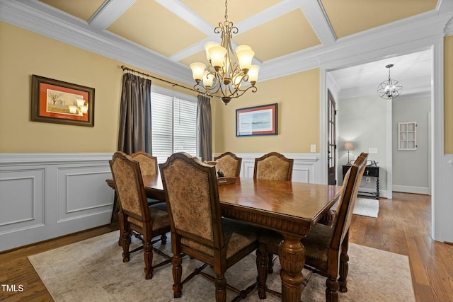 dining area with coffered ceiling, a notable chandelier, crown molding, and light hardwood / wood-style flooring