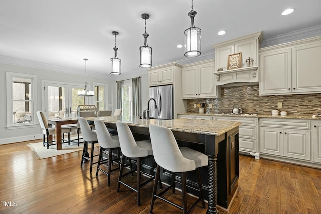 kitchen with hanging light fixtures, an island with sink, stainless steel fridge, and crown molding