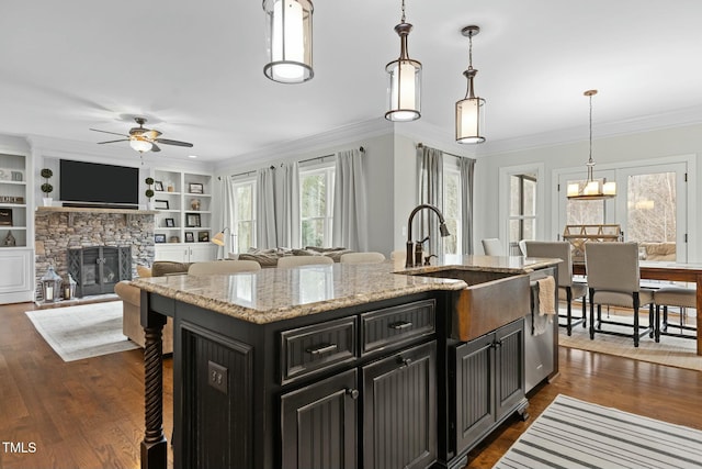 kitchen with pendant lighting, dishwasher, light stone counters, a center island with sink, and built in shelves