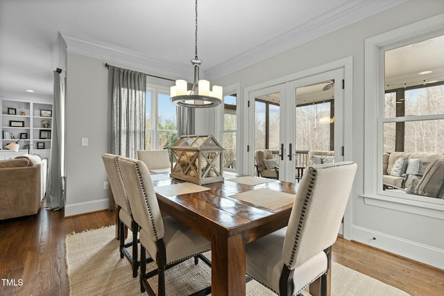 dining space with french doors, crown molding, built in features, a notable chandelier, and hardwood / wood-style floors