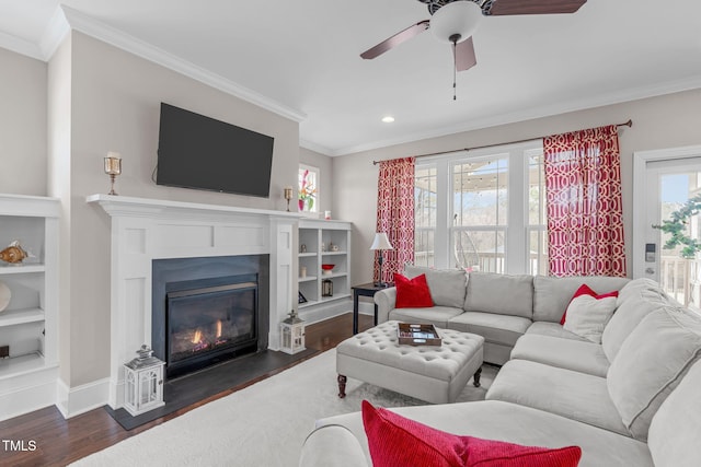 living area with baseboards, a fireplace with flush hearth, ceiling fan, ornamental molding, and dark wood-type flooring