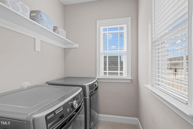 clothes washing area with laundry area, washing machine and clothes dryer, a wealth of natural light, and baseboards