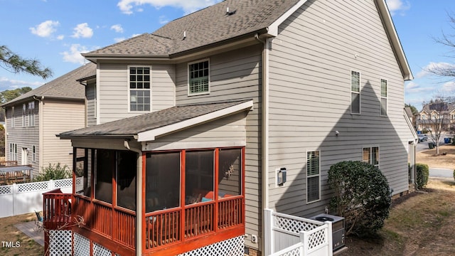 back of property with central AC unit, fence, a sunroom, and a shingled roof