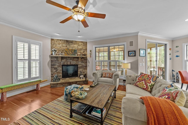 living area featuring wood finished floors, baseboards, a ceiling fan, a fireplace, and crown molding