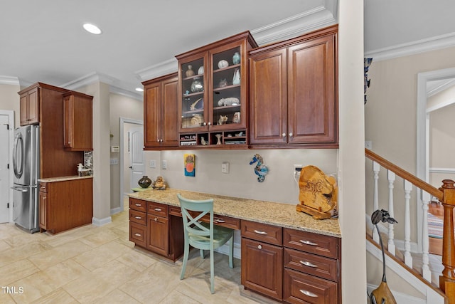 kitchen with light stone countertops, ornamental molding, built in desk, and freestanding refrigerator