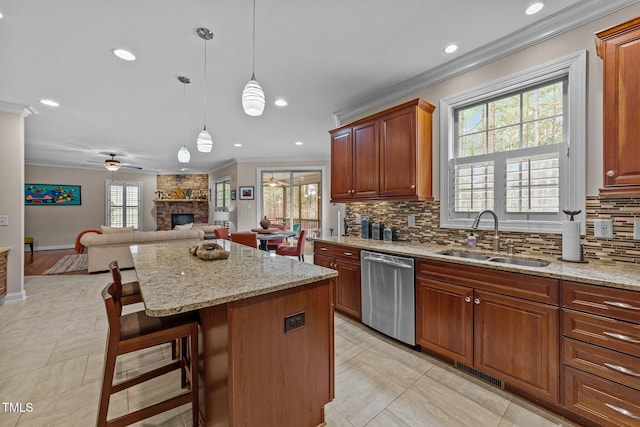 kitchen with open floor plan, ornamental molding, a stone fireplace, stainless steel dishwasher, and a sink