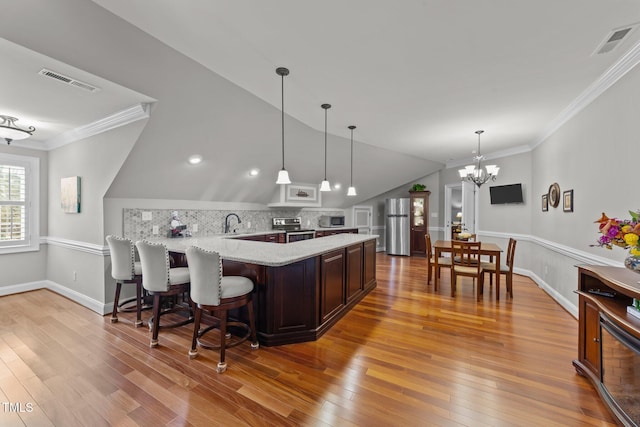 kitchen featuring kitchen peninsula, appliances with stainless steel finishes, a breakfast bar, ornamental molding, and lofted ceiling