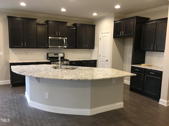 kitchen featuring light stone counters, dark wood-type flooring, stainless steel appliances, and a center island with sink