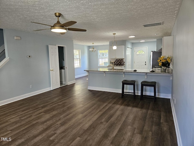 kitchen with a kitchen bar, stainless steel refrigerator, white cabinets, decorative light fixtures, and kitchen peninsula