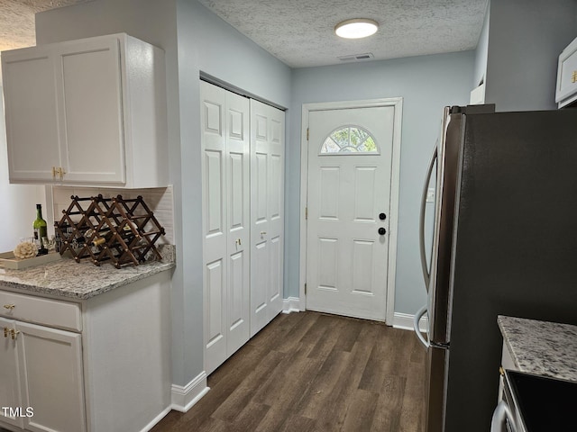 kitchen featuring a textured ceiling, white cabinets, stainless steel fridge, dark hardwood / wood-style floors, and light stone counters