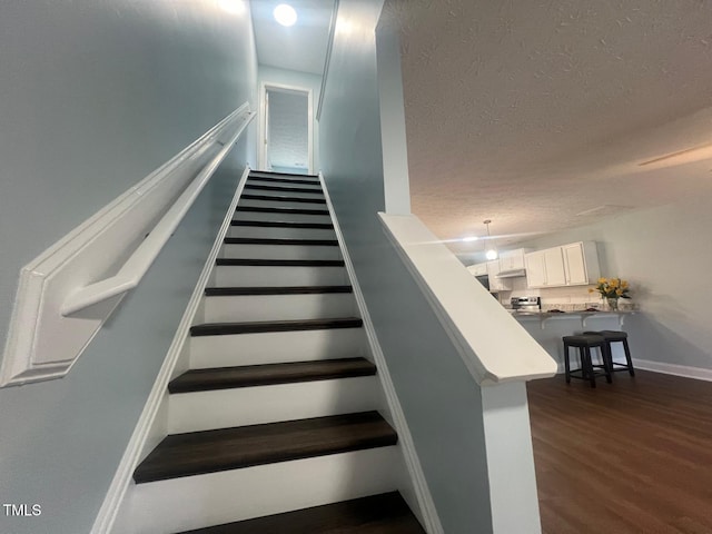 stairway with a textured ceiling and hardwood / wood-style floors