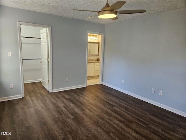 unfurnished bedroom with a textured ceiling, a walk in closet, a closet, ceiling fan, and dark hardwood / wood-style floors