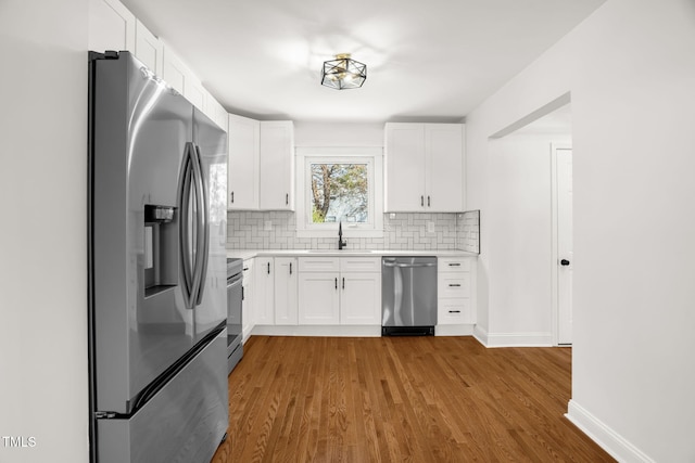 kitchen featuring sink, appliances with stainless steel finishes, backsplash, hardwood / wood-style floors, and white cabinets