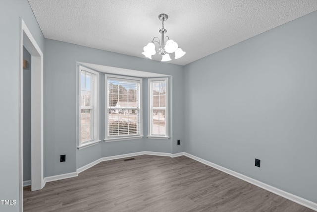 unfurnished dining area featuring hardwood / wood-style flooring, a textured ceiling, and a chandelier