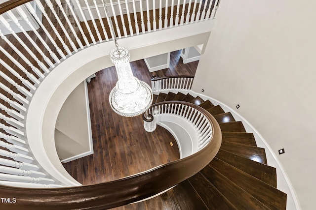 staircase featuring wood-type flooring, a towering ceiling, and a chandelier