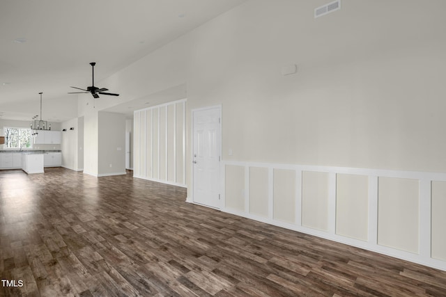 unfurnished living room featuring vaulted ceiling, ceiling fan with notable chandelier, and dark hardwood / wood-style floors