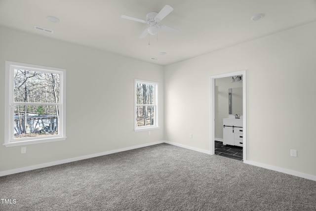 unfurnished bedroom featuring ceiling fan, dark carpet, connected bathroom, and multiple windows