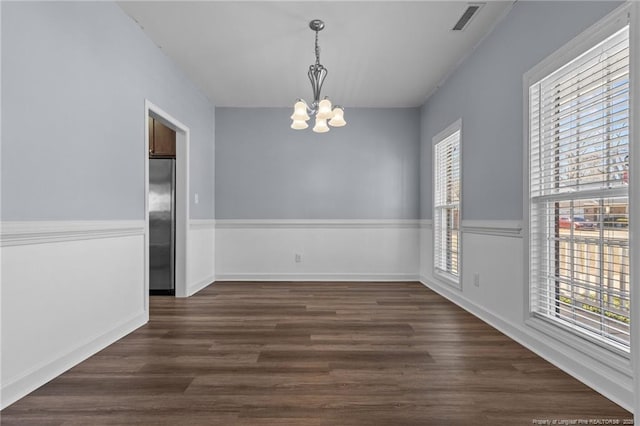 unfurnished room with a notable chandelier, a wealth of natural light, and dark hardwood / wood-style floors