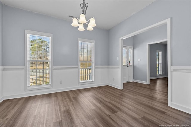 unfurnished dining area with dark wood-type flooring, a notable chandelier, and a healthy amount of sunlight