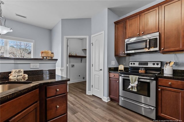 kitchen with decorative light fixtures, sink, dark stone counters, appliances with stainless steel finishes, and dark hardwood / wood-style floors