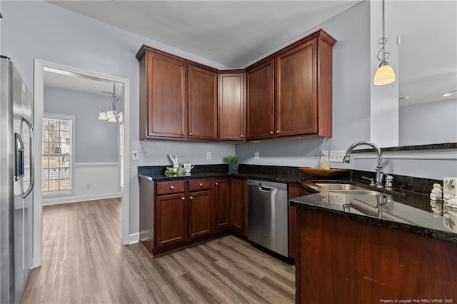 kitchen featuring hanging light fixtures, stainless steel appliances, light hardwood / wood-style flooring, sink, and dark stone counters