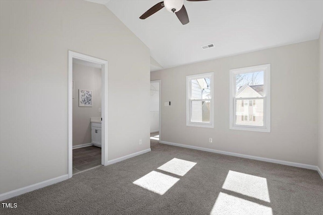 unfurnished bedroom with lofted ceiling, connected bathroom, dark carpet, and ceiling fan