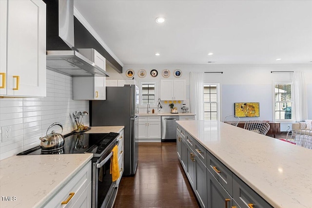 kitchen featuring gray cabinetry, light stone counters, appliances with stainless steel finishes, wall chimney range hood, and white cabinets