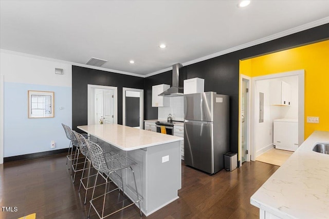 kitchen with white cabinetry, a breakfast bar area, a center island, stainless steel appliances, and wall chimney range hood