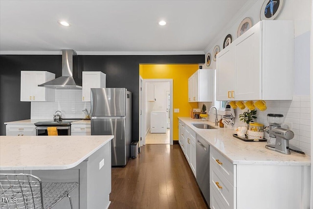 kitchen with wall chimney range hood, sink, appliances with stainless steel finishes, white cabinets, and a kitchen bar