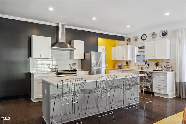 kitchen with a center island, appliances with stainless steel finishes, dark hardwood / wood-style flooring, wall chimney range hood, and white cabinets