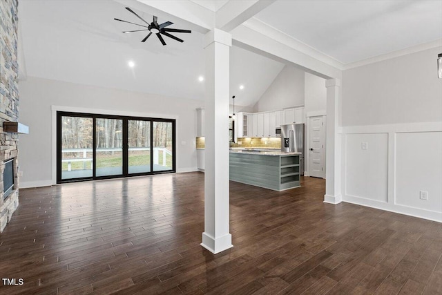 unfurnished living room featuring ceiling fan, high vaulted ceiling, decorative columns, a fireplace, and dark hardwood / wood-style flooring