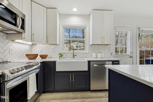 kitchen featuring sink, white cabinetry, tasteful backsplash, light stone counters, and appliances with stainless steel finishes