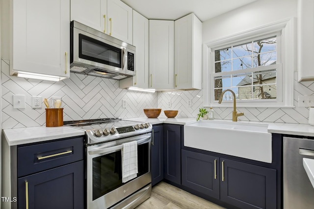 kitchen with sink, white cabinetry, light stone counters, stainless steel appliances, and decorative backsplash